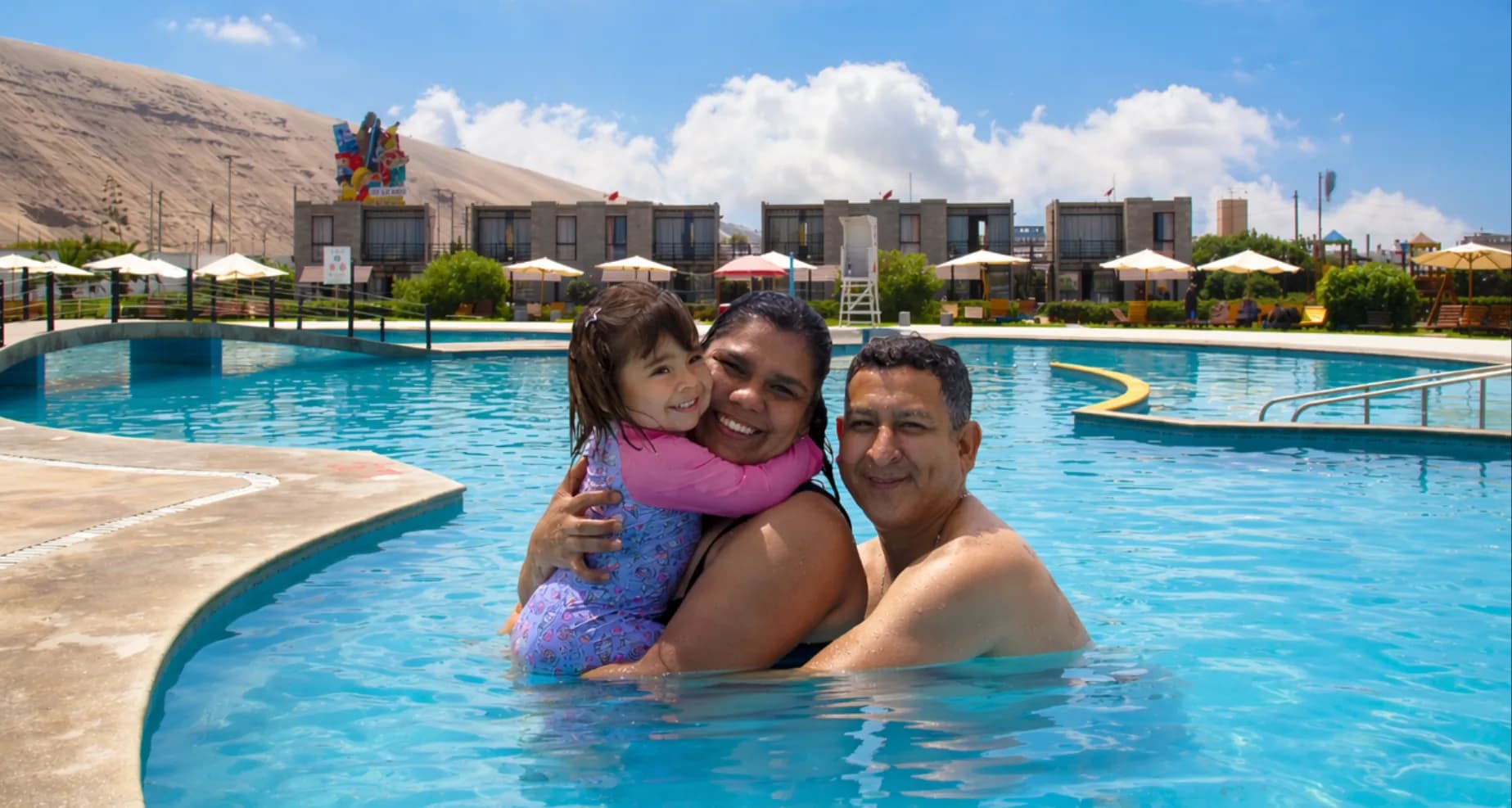 Familia disfrutando la piscina de Touricamp Lurín con bungalows y duna al fondo